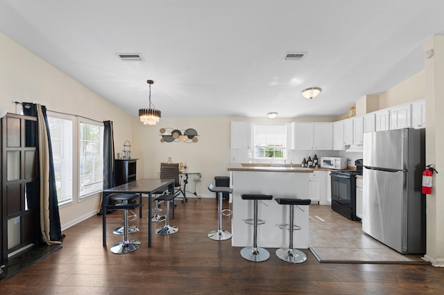716 21st St, West Palm Beach, FL 33407 - kitchen featuring freestanding refrigerator, black range with electric stovetop, white microwave, a breakfast bar area, and white cabinets