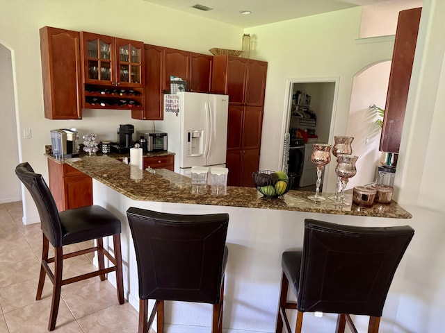 1710 SW Columbia St, Port Saint Lucie, FL 34987 - kitchen with white refrigerator with ice dispenser, dark stone countertops, a peninsula, glass insert cabinets, and a breakfast bar
