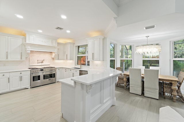 106 Henry Sewall Way, Sewalls Point, FL 34996 - kitchen featuring appliances with stainless steel finishes, a chandelier, white cabinets, a peninsula, and backsplash