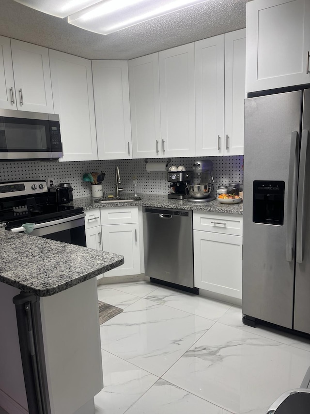 4988 Sable Pine Cir Unit B2, West Palm Beach, FL 33417 - kitchen featuring appliances with stainless steel finishes, a sink, light marble finish floors, white cabinetry, and dark stone counters