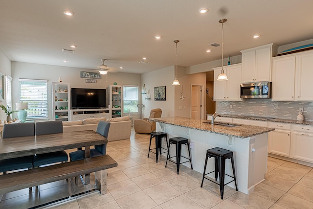 9351 SW Serapis Way, Port Saint Lucie, FL 34987 - kitchen featuring stainless steel microwave, a sink, backsplash, stone counters, and a breakfast bar area