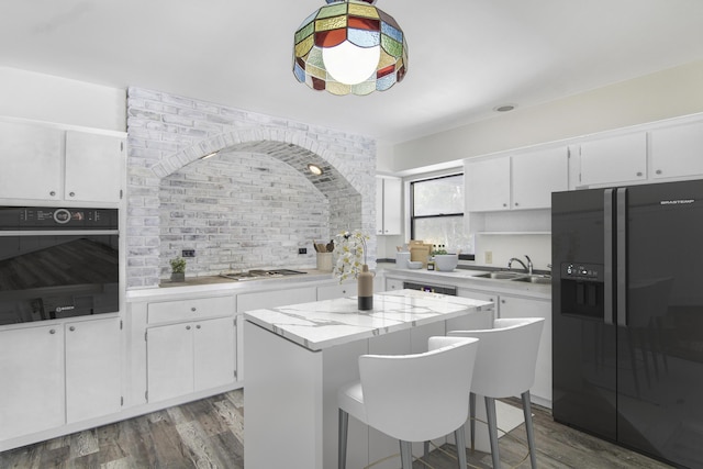 5666 SE Matousek St, Stuart, FL 34997 - kitchen featuring black refrigerator with ice dispenser, wall oven, a sink, wood finished floors, and a center island