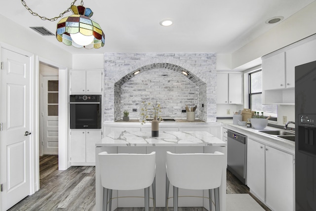 5666 SE Matousek St, Stuart, FL 34997 - kitchen with black oven, stainless steel dishwasher, a sink, white cabinetry, and decorative backsplash
