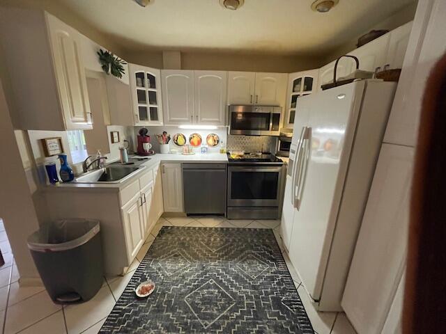 108 SW 18th St, Boynton Beach, FL 33426 - kitchen featuring stainless steel appliances, a sink, light tile patterned floors, glass insert cabinets, and white cabinets