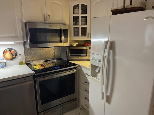 108 SW 18th St, Boynton Beach, FL 33426 - kitchen featuring appliances with stainless steel finishes, light countertops, decorative backsplash, white cabinetry, and glass insert cabinets