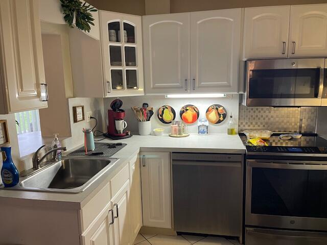 108 SW 18th St, Boynton Beach, FL 33426 - kitchen featuring stainless steel appliances, a sink, light countertops, glass insert cabinets, and tasteful backsplash