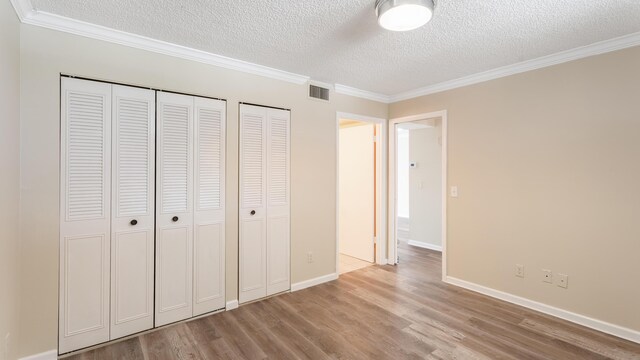 1950 SW Palm City Rd Unit 8302, Stuart, FL 34994 - unfurnished bedroom with a textured ceiling, ornamental molding, light wood finished floors, two closets, and baseboards