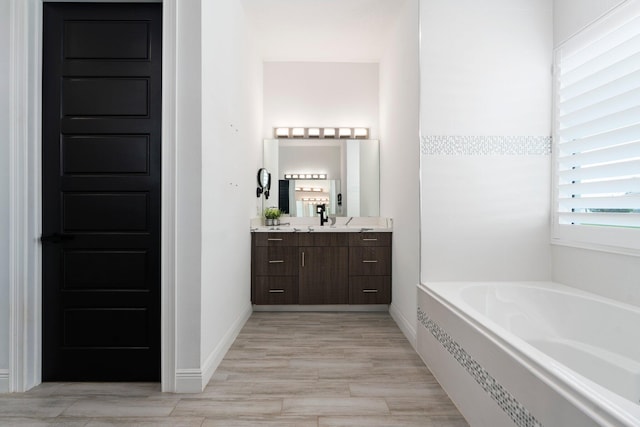 979 SW Mcdevitt Ave, Port Saint Lucie, FL 34953 - bathroom featuring a garden tub, vanity, wood finished floors, and baseboards