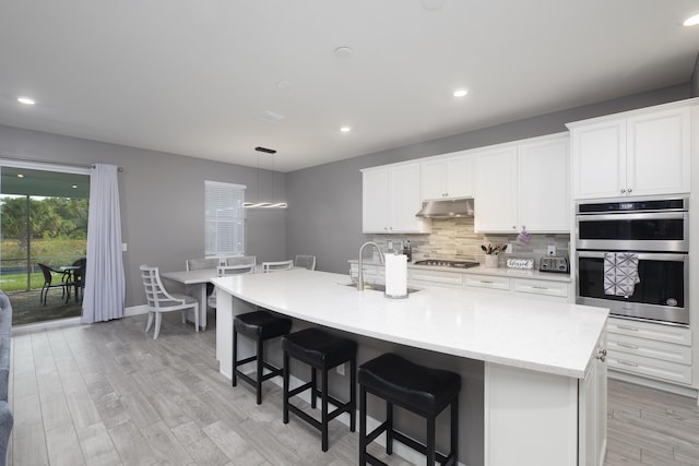 10299 SW Captiva Dr, Port Saint Lucie, FL 34987 - kitchen featuring stainless steel double oven, a sink, under cabinet range hood, gas stovetop, and backsplash