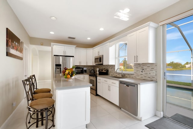 9461 Aegean Dr, Boca Raton, FL 33496 - kitchen featuring appliances with stainless steel finishes, a sink, backsplash, a kitchen bar, and white cabinetry