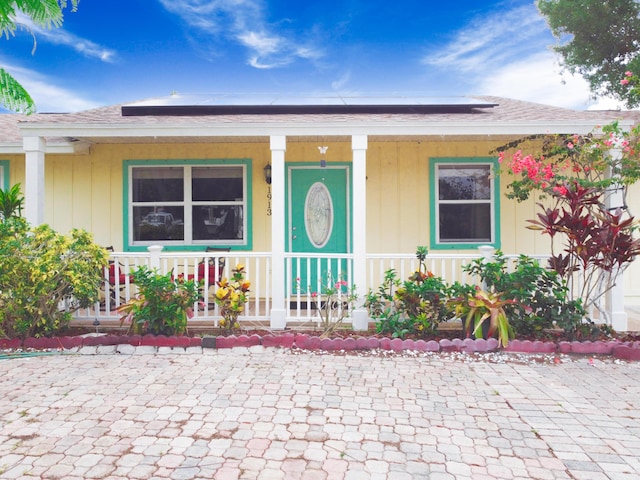 1913 SW Idaho Ln, Port Saint Lucie, FL 34953 - doorway to property with covered porch, solar panels, and roof with shingles