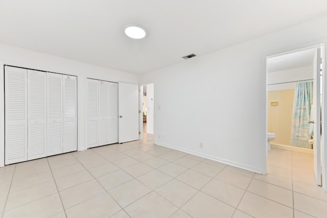 522 Evergreen Dr, Lake Park, FL 33403 - unfurnished bedroom with multiple closets, baseboards, light tile patterned flooring, and connected bathroom