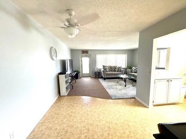 127 Berkshire F, West Palm Beach, FL 33417 - living area with a textured ceiling, a ceiling fan, baseboards, light colored carpet, and light floors
