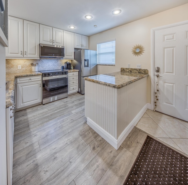 1428 S Lakeside Dr Unit 31, Lake Worth Beach, FL 33460 - kitchen featuring appliances with stainless steel finishes, a peninsula, white cabinetry, light stone counters, and light wood-type flooring