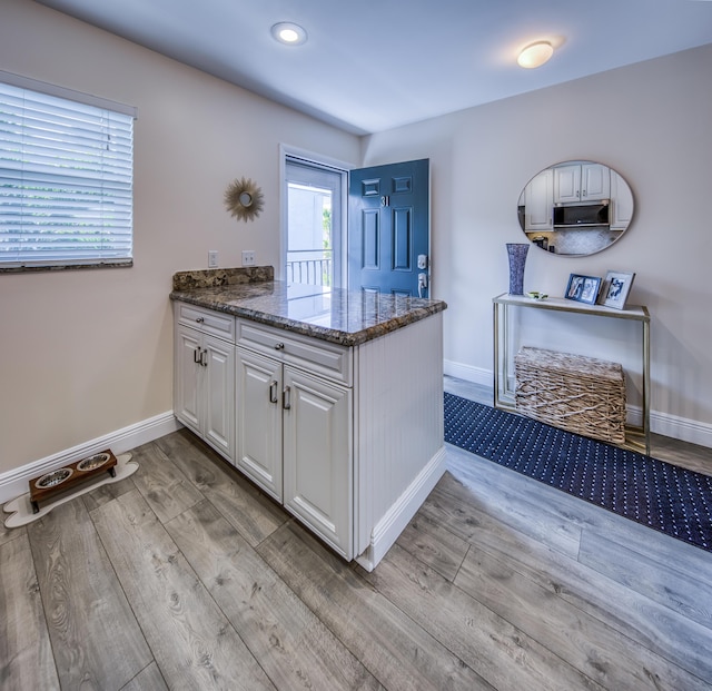1428 S Lakeside Dr Unit 31, Lake Worth Beach, FL 33460 - kitchen with white cabinets, wood finished floors, dark stone counters, baseboards, and stainless steel microwave