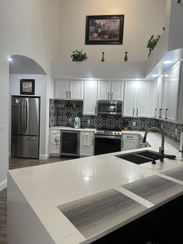 1583 SW Harbour Isles Cir Unit 57, Port Saint Lucie, FL 34986 - kitchen with appliances with stainless steel finishes, wine cooler, a sink, a high ceiling, and light stone counters