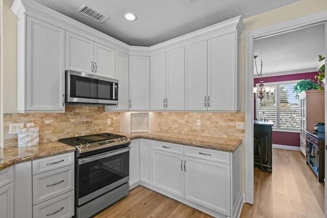 256 Coconut Pt, Jupiter, FL 33458 - kitchen with stainless steel appliances, white cabinetry, light wood-style flooring, a chandelier, and a textured ceiling