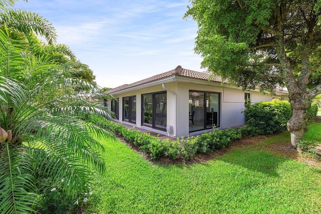 4483 Meadowlark Ln, Boynton Beach, FL 33436 - view of side of home with stucco siding, a tiled roof, a yard, and a sunroom