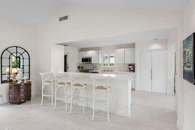 4483 Meadowlark Ln, Boynton Beach, FL 33436 - kitchen with appliances with stainless steel finishes, a breakfast bar, light countertops, a peninsula, and high vaulted ceiling