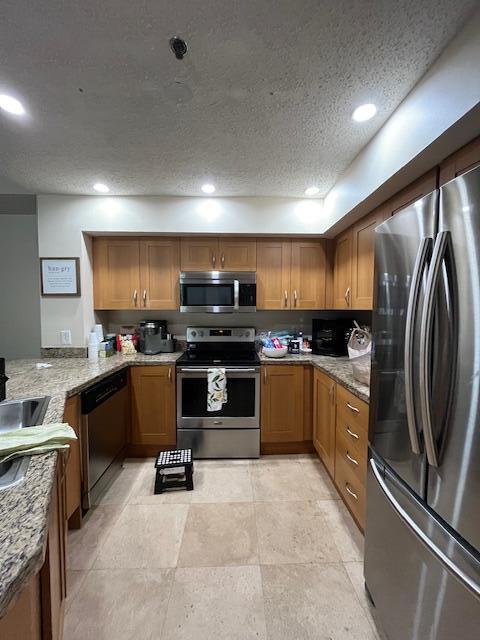3153 Clint Moore Rd Unit 204, Boca Raton, FL 33496 - kitchen with appliances with stainless steel finishes, a textured ceiling, brown cabinetry, light stone countertops, and recessed lighting
