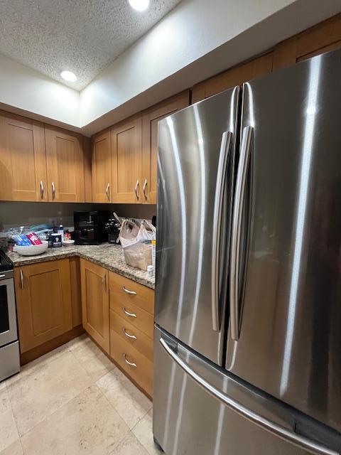 3153 Clint Moore Rd Unit 204, Boca Raton, FL 33496 - kitchen featuring appliances with stainless steel finishes, brown cabinets, a textured ceiling, light stone countertops, and recessed lighting