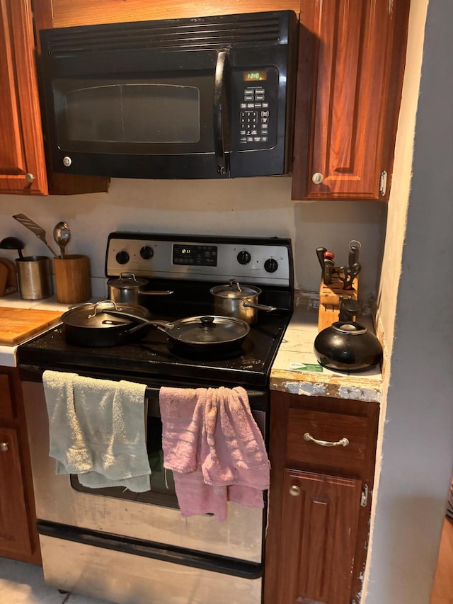 8587 SW 18th Ave, Stuart, FL 34997 - kitchen with stainless steel electric range oven, black microwave, light countertops, and brown cabinetry