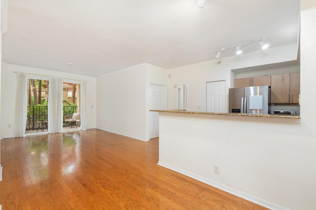 1801 N Flagler Dr Unit 107, West Palm Beach, FL 33407 - unfurnished living room featuring light wood-style flooring, baseboards, rail lighting, and a textured ceiling