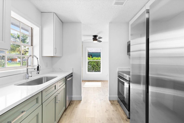 6681 4th St, Jupiter, FL 33458 - kitchen featuring appliances with stainless steel finishes, a sink, light wood finished floors, plenty of natural light, and a textured ceiling