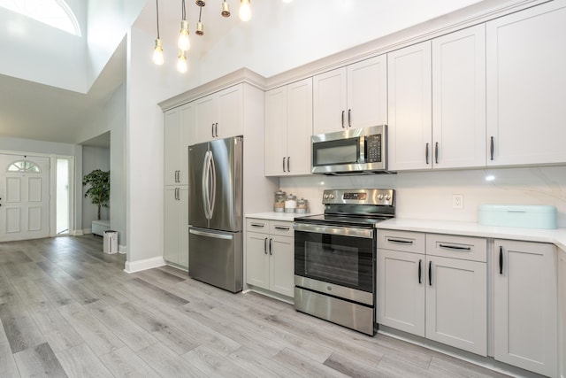 17069 81st Ln N, Loxahatchee, FL 33470 - kitchen featuring appliances with stainless steel finishes, a high ceiling, light countertops, light wood-type flooring, and pendant lighting