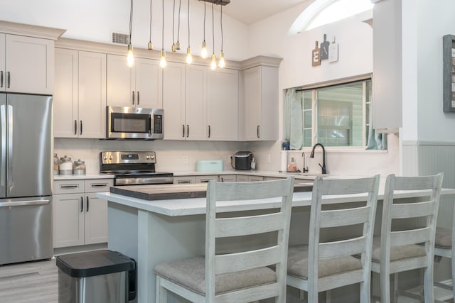 17069 81st Ln N, Loxahatchee, FL 33470 - kitchen featuring stainless steel appliances, a kitchen bar, light countertops, decorative light fixtures, and light wood-style floors