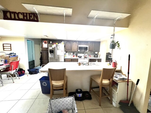 125 Capri Ave, Sebastian, FL 32958 - kitchen with stainless steel fridge with ice dispenser, light tile patterned flooring, light countertops, a kitchen bar, and a sink