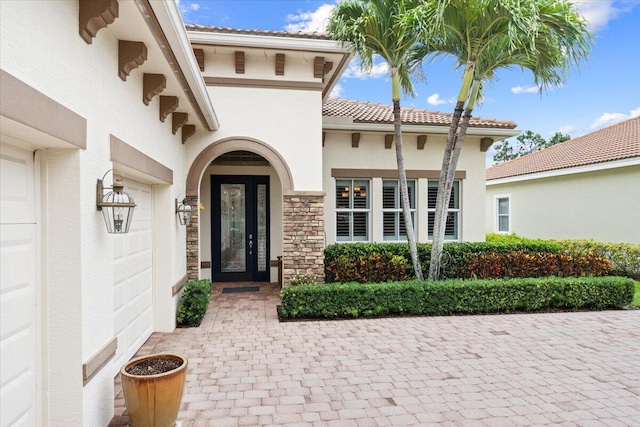 9926 SW Nuova Way, Port Saint Lucie, FL 34986 - view of exterior entry with stucco siding, stone siding, an attached garage, and a tiled roof