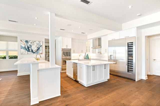 18119 SE Federal Hwy, Tequesta, FL 33469 - kitchen featuring built in fridge, an island with sink, stainless steel double oven, wall chimney exhaust hood, and white cabinets