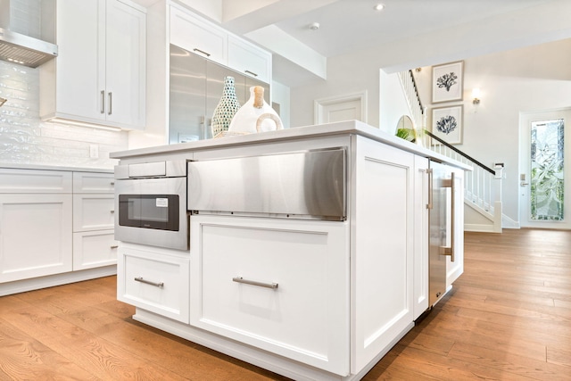 18119 SE Federal Hwy, Tequesta, FL 33469 - kitchen featuring light wood finished floors, white cabinets, wall chimney exhaust hood, backsplash, and light countertops