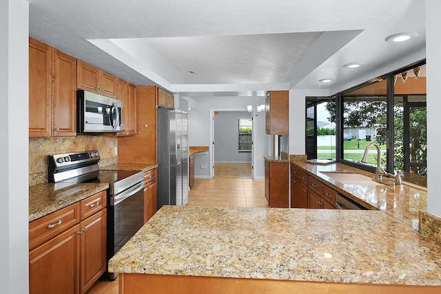 515 SE Nome Dr, Port Saint Lucie, FL 34984 - kitchen with stainless steel appliances, a sink, light tile patterned flooring, brown cabinetry, and decorative backsplash
