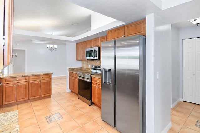 515 SE Nome Dr, Port Saint Lucie, FL 34984 - kitchen featuring stainless steel appliances, light tile patterned floors, brown cabinets, decorative backsplash, and a chandelier