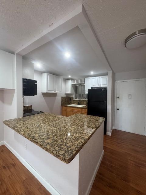 6080 Forest Hill Blvd Unit 201, West Palm Beach, FL 33415 - kitchen with freestanding refrigerator, a peninsula, dark wood finished floors, dark stone counters, and a textured ceiling