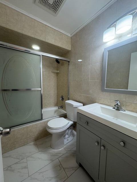 6080 Forest Hill Blvd Unit 201, West Palm Beach, FL 33415 - bathroom with tile walls, combined bath / shower with glass door, vanity, ornamental molding, and toilet