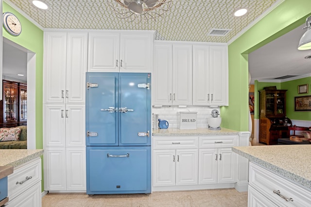 4633 Holly Dr, Palm Beach Gardens, FL 33418 - kitchen with white cabinets, paneled fridge, crown molding, recessed lighting, and light stone counters