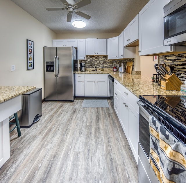 1516 S Lakeside Dr Unit 205, Lake Worth Beach, FL 33460 - kitchen with appliances with stainless steel finishes, light wood-style floors, a ceiling fan, backsplash, and a textured ceiling
