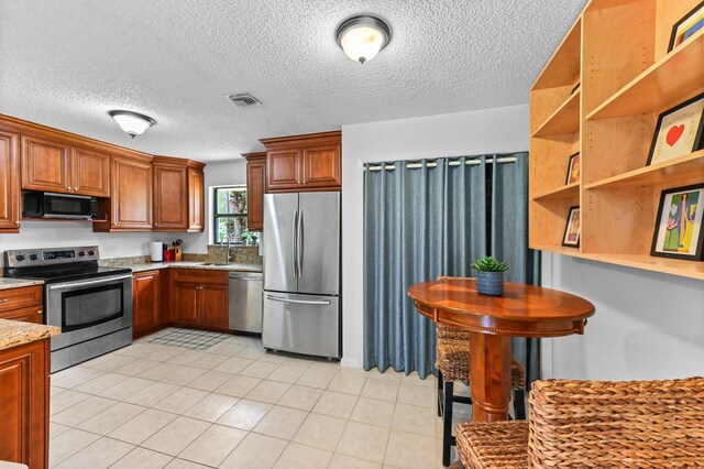 17183 76th St N, Loxahatchee, FL 33470 - kitchen with stainless steel appliances, a sink, brown cabinetry, light stone counters, and a textured ceiling