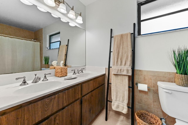 17183 76th St N, Loxahatchee, FL 33470 - full bath with double vanity, tile patterned flooring, toilet, tile walls, and a wainscoted wall