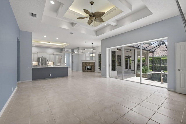 19050 SE Kokomo Ln, Jupiter, FL 33458 - unfurnished living room with a tray ceiling, ceiling fan, a towering ceiling, light tile patterned flooring, and a fireplace