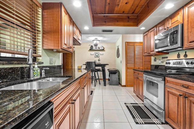 129 Parkwood Dr, Royal Palm Beach, FL 33411 - kitchen with stainless steel appliances, a raised ceiling, a sink, light tile patterned flooring, and brown cabinetry