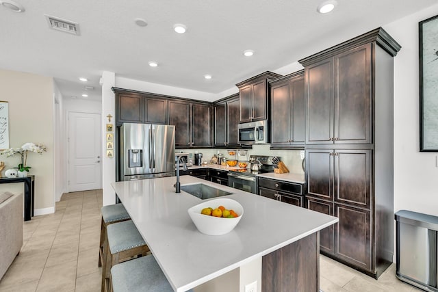 4340 Lago Dr, Deerfield Beach, FL 33064 - kitchen with appliances with stainless steel finishes, a sink, light tile patterned flooring, dark brown cabinets, and an island with sink