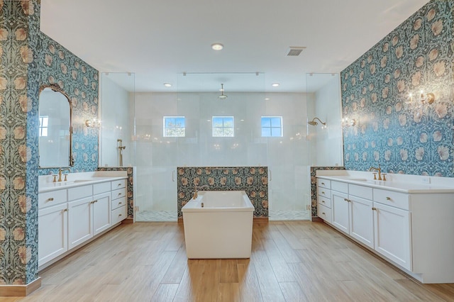 10032 Calabrese Trl, Jupiter, FL 33478 - bathroom with wallpapered walls, a walk in shower, two vanities, wood finished floors, and a soaking tub