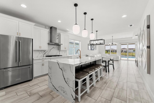 11244 SW Lyra Dr, Port Saint Lucie, FL 34987 - kitchen with high end fridge, wall chimney range hood, gas cooktop, an island with sink, and white cabinets