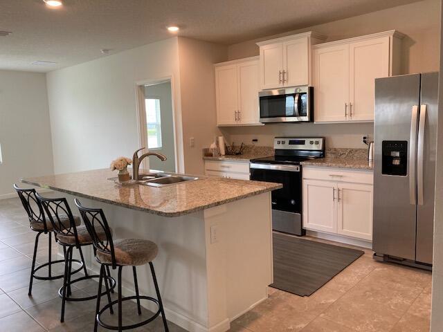 10789 SW Cremona Way, Port Saint Lucie, FL 34987 - kitchen featuring stainless steel appliances, a kitchen island with sink, white cabinets, light tile patterned flooring, and light stone counters