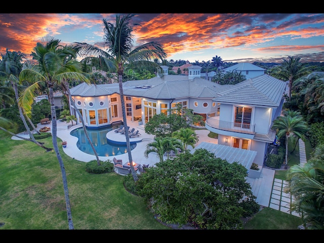 12990 Marsh Lndg, Palm Beach Gardens, FL 33418 - back of house at dusk with a balcony, a patio, an outdoor pool, stucco siding, and a tile roof