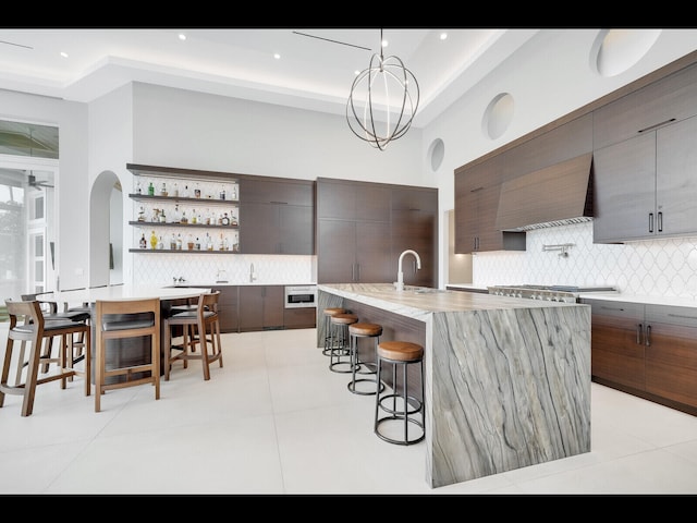 12990 Marsh Lndg, Palm Beach Gardens, FL 33418 - kitchen featuring modern cabinets, a breakfast bar, decorative backsplash, open shelves, and a kitchen island with sink